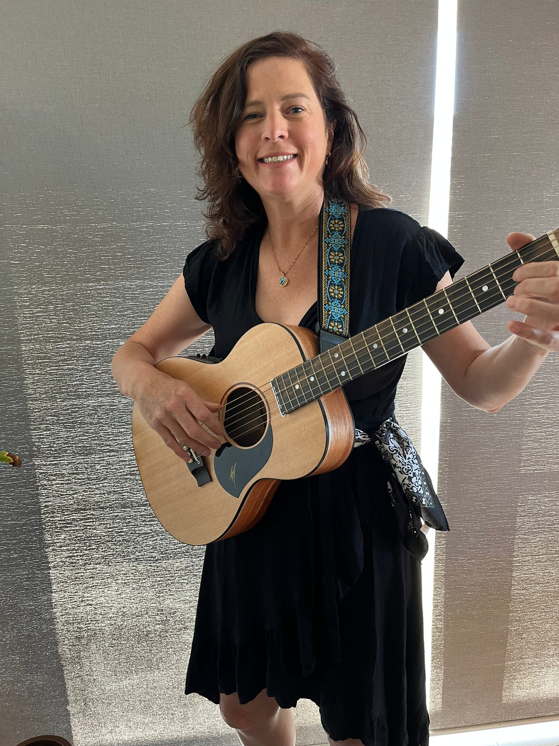 Caroline standing and holding an acoustic guitar.  She is wearing a black dress and has her hair down.  She has a small smile on her face. 