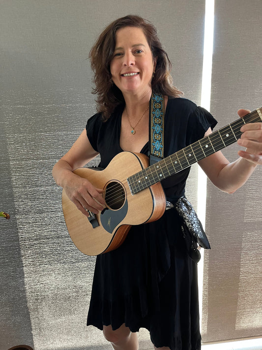 Caroline standing and holding an acoustic guitar.  She is wearing a black dress and has her hair down.  She has a small smile on her face. 
